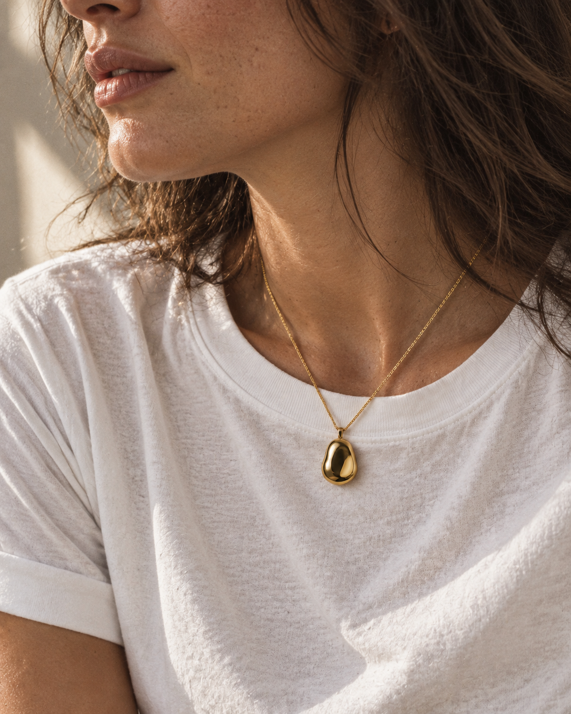Editorial concept: small rounded gold pendant against a white T-shirt in side light