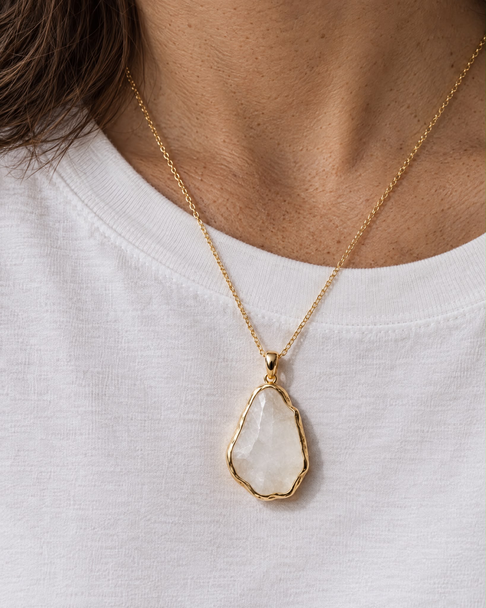 White T-shirt with a pale stone pendant on a fine gold chain