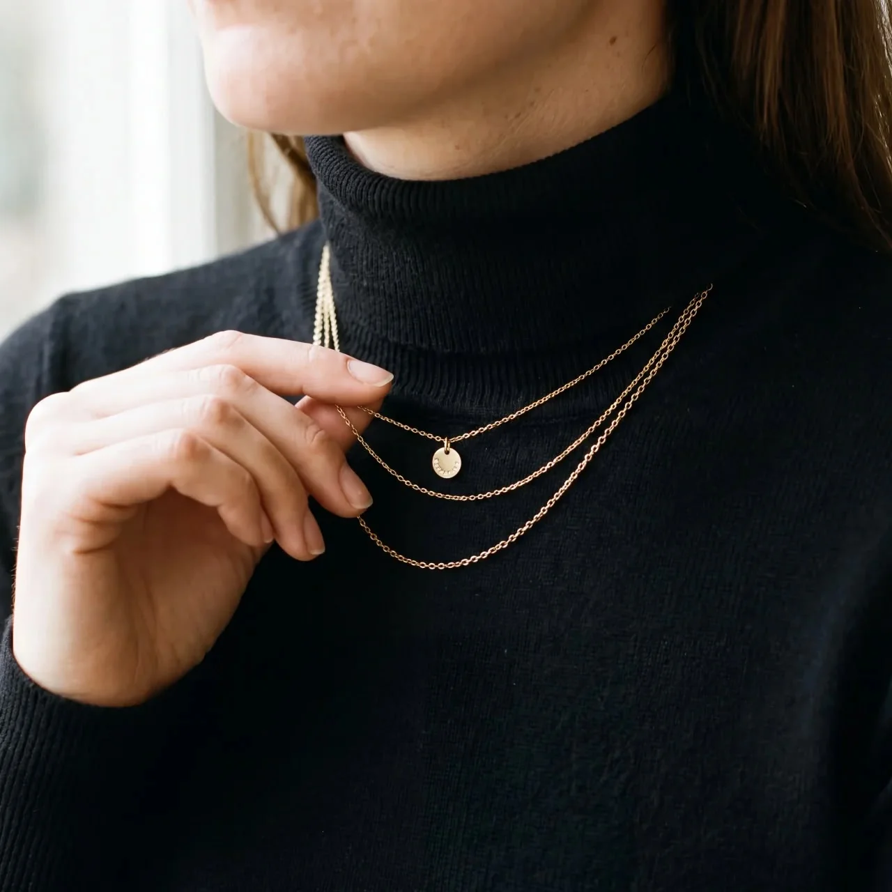 Three gold necklace layers over a black turtleneck